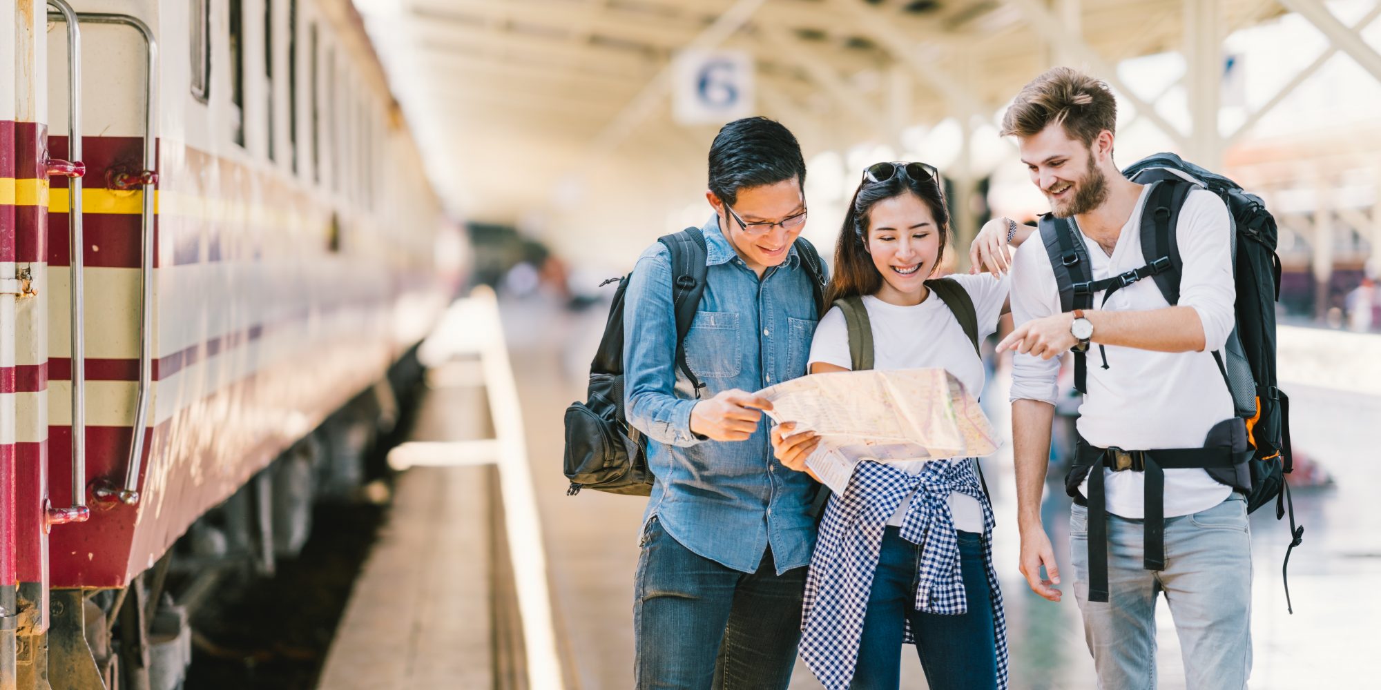 Multiethnic group of friends backpack travelers or college students using local map navigation together at train station platform. Asia travel destination tourism activity or railroad trip concept
